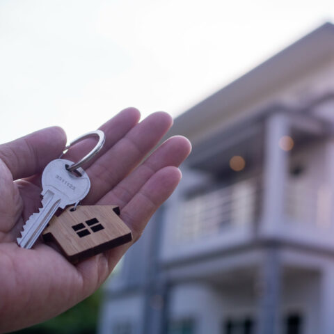 Eine Hand hält einen Schlüssel - im Hintergrund unscharf ein Haus.