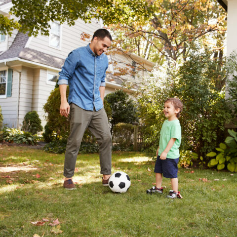 Vater und Sohn spielen Ball in einem Garten.